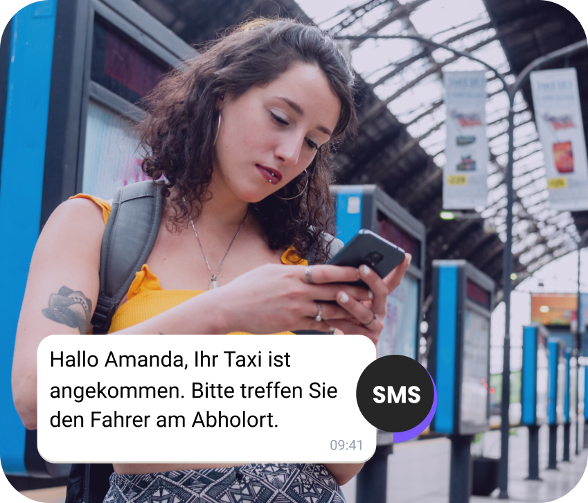 Reisende mit Rucksack am Bahnhof liest eine SMS über ihr ankommendes Taxi.